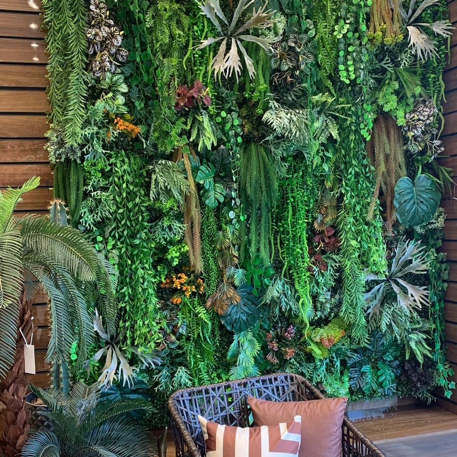 Jardim vertical permanente de folhagens mescladas cobrindo uma parede inteira, com poltrona à frente